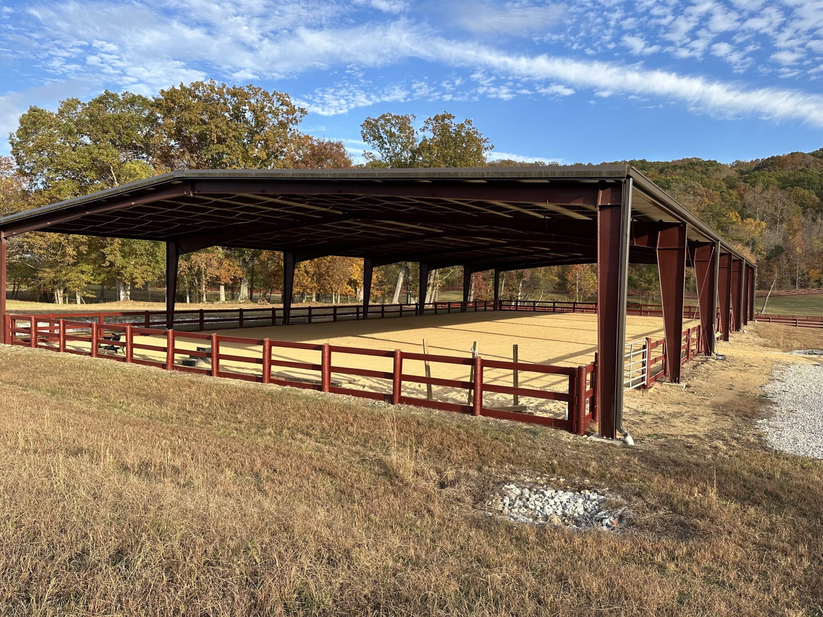 A large open area with a fence and a covered riding arena.